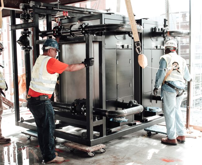 three workers holding parts of mechanical penthouse and installing